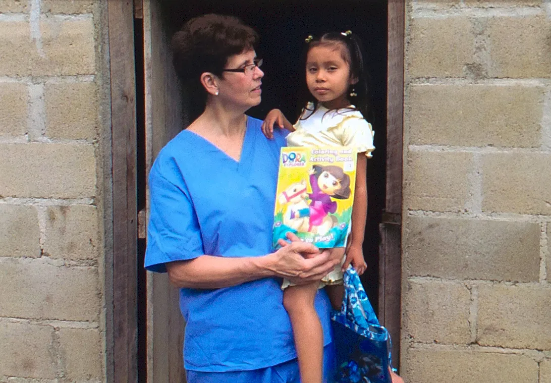 A Smiles Bring Hope clinician in blue scrubs holding a young child during the 2014 Belize mission